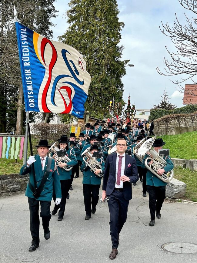 Der Fähnrich und Dirigent der Ortsmusik Rüediswil schreiten voran